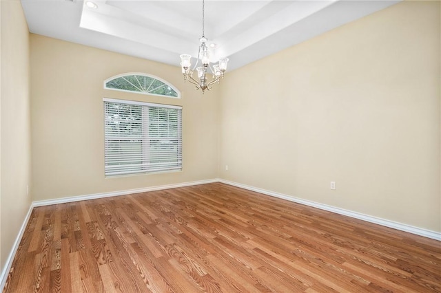 empty room with hardwood / wood-style flooring, a chandelier, and a tray ceiling