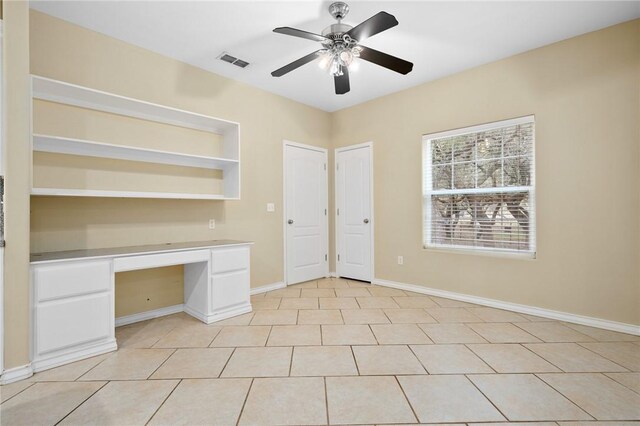 unfurnished office with built in desk, ceiling fan, and light tile patterned floors