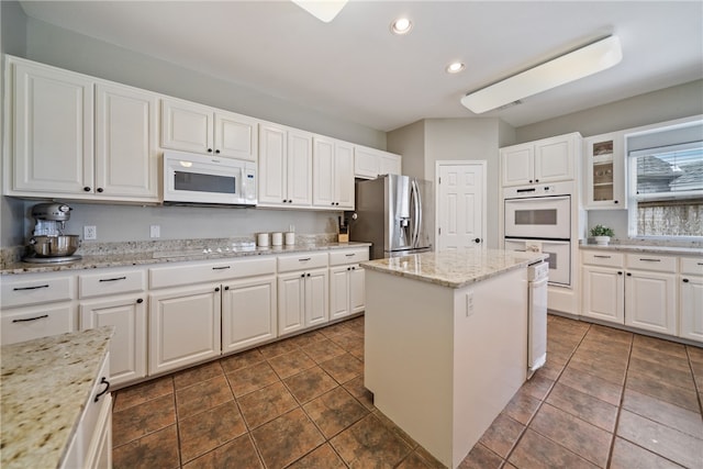 kitchen featuring a center island, white appliances, light stone counters, and white cabinets