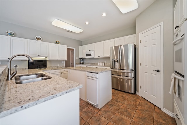 kitchen with light stone counters, a center island, sink, white cabinetry, and white appliances