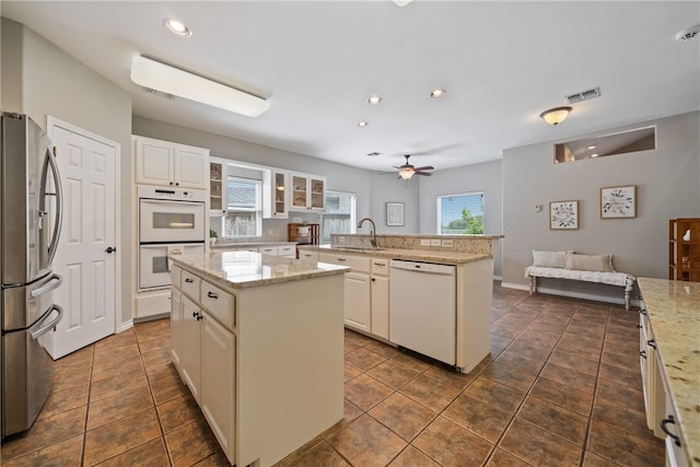 kitchen featuring ceiling fan, white appliances, a kitchen island, and light stone countertops