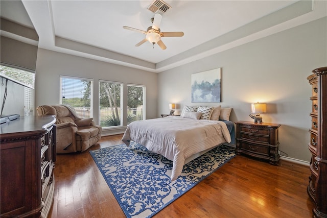 bedroom with dark wood-type flooring, a tray ceiling, and ceiling fan