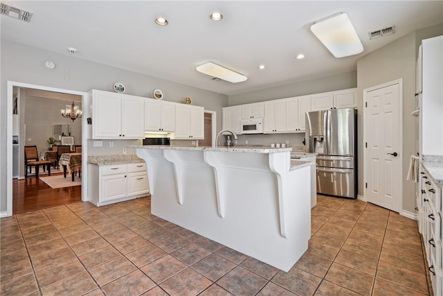 kitchen featuring white cabinetry, a center island with sink, light stone counters, and stainless steel fridge