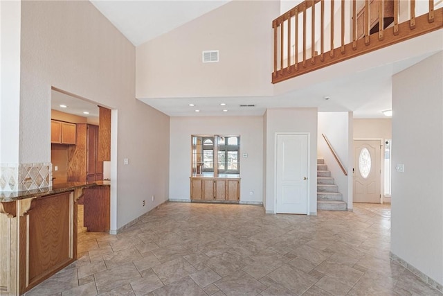 unfurnished living room with high vaulted ceiling, visible vents, stairway, and baseboards