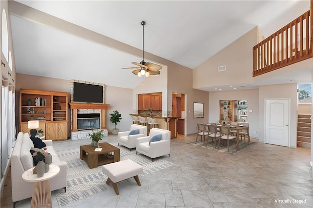 living area featuring visible vents, ceiling fan, stairway, vaulted ceiling, and a stone fireplace