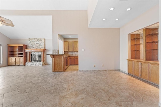 unfurnished living room with a stone fireplace, recessed lighting, a ceiling fan, and baseboards