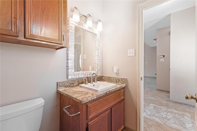 half bathroom featuring toilet, baseboards, and vanity