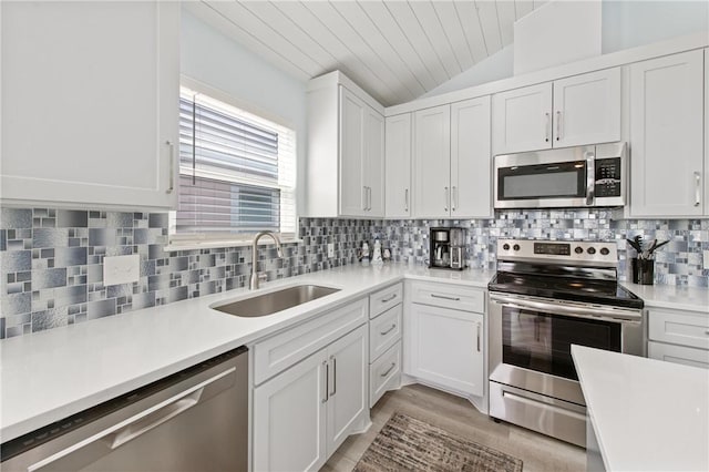 kitchen featuring sink, vaulted ceiling, stainless steel appliances, decorative backsplash, and white cabinets