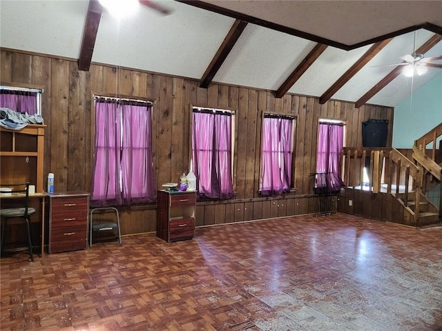 unfurnished living room featuring dark parquet floors, ceiling fan, wooden walls, lofted ceiling with beams, and plenty of natural light