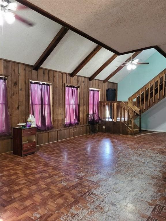 unfurnished living room with ceiling fan, parquet floors, vaulted ceiling with beams, wood walls, and a textured ceiling