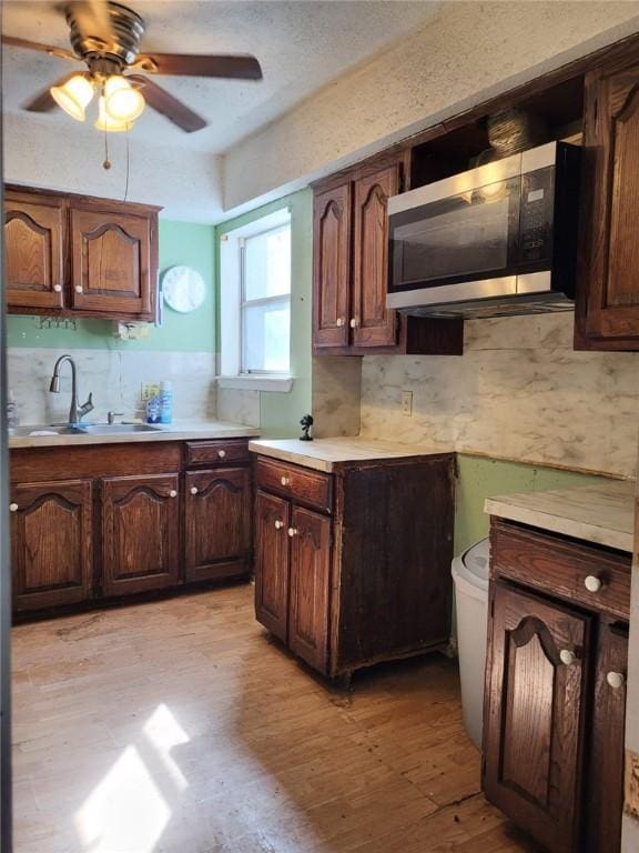 kitchen featuring light wood-type flooring, backsplash, dark brown cabinets, ceiling fan, and sink