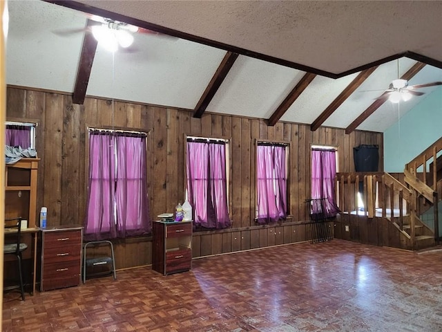 unfurnished living room featuring ceiling fan, vaulted ceiling with beams, dark parquet floors, wood walls, and a textured ceiling