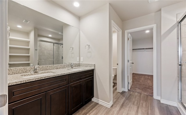 full bathroom featuring a walk in closet, toilet, a stall shower, a sink, and wood finished floors