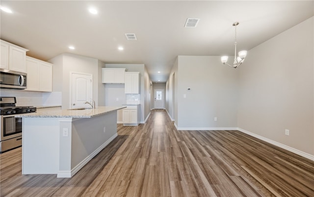 kitchen featuring stainless steel appliances, visible vents, white cabinetry, an island with sink, and light stone countertops