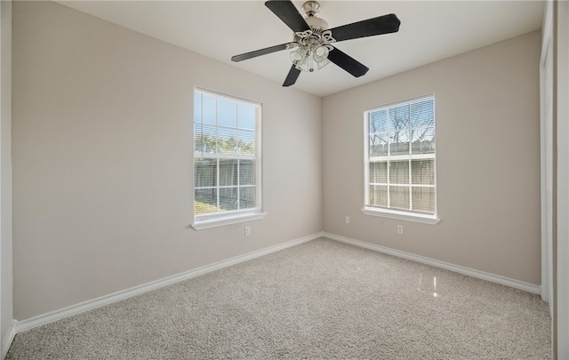 carpeted spare room featuring a wealth of natural light, ceiling fan, and baseboards