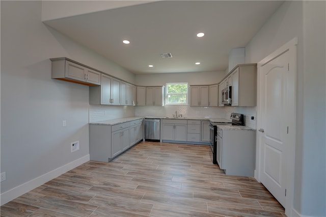 kitchen with gray cabinetry, appliances with stainless steel finishes, light stone countertops, decorative backsplash, and light hardwood / wood-style floors