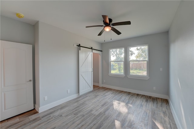 unfurnished bedroom featuring light hardwood / wood-style floors, a barn door, and ceiling fan