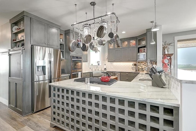 kitchen with tasteful backsplash, kitchen peninsula, pendant lighting, stainless steel appliances, and light stone countertops