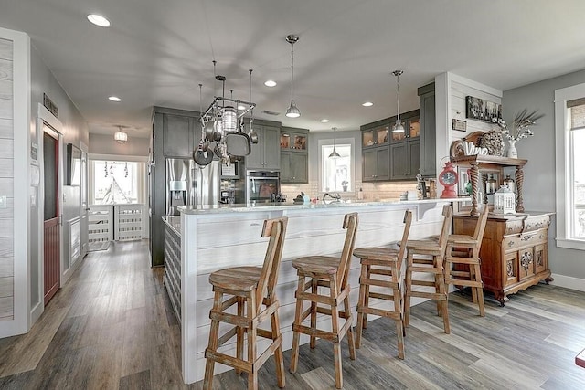 kitchen featuring appliances with stainless steel finishes, kitchen peninsula, wood-type flooring, and backsplash