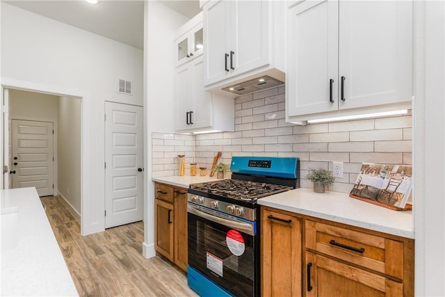 2513 Luzius Dr, Corpus Christi, TX 78418 - kitchen featuring stainless steel gas range oven, light countertops, white cabinets, light wood-style flooring, and backsplash