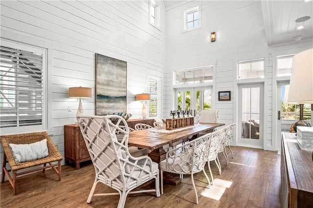 dining room featuring french doors, wooden walls, hardwood / wood-style flooring, and a high ceiling