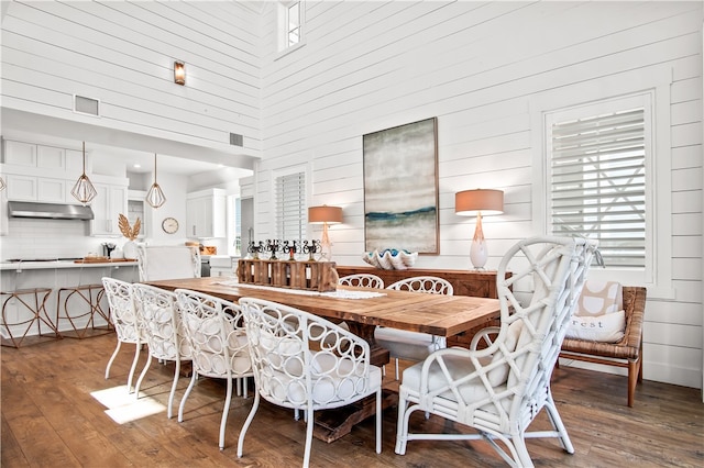 dining room with wood walls, hardwood / wood-style flooring, and a high ceiling