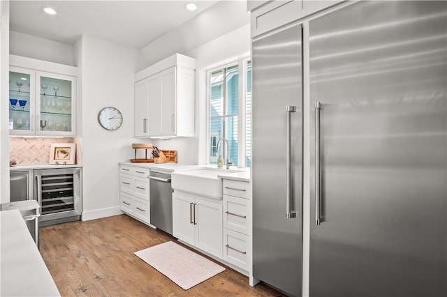 kitchen with light wood-type flooring, beverage cooler, white cabinets, and stainless steel appliances