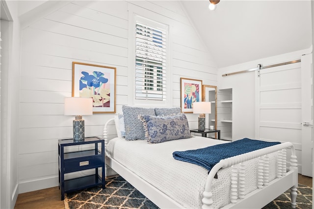 bedroom featuring wooden walls, a barn door, vaulted ceiling, and dark hardwood / wood-style floors