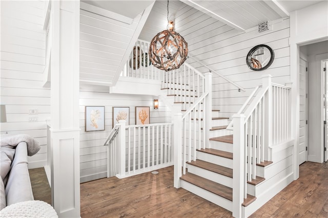 staircase with an inviting chandelier, beamed ceiling, wooden walls, and wood-type flooring