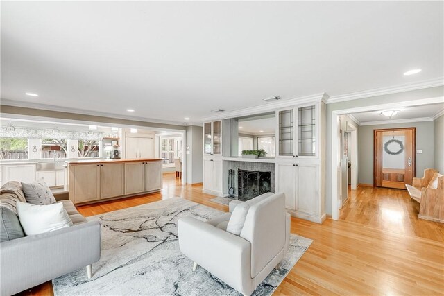 living room with ornamental molding, light wood-type flooring, a brick fireplace, and recessed lighting