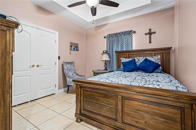 bedroom featuring a raised ceiling, light tile patterned floors, and ceiling fan