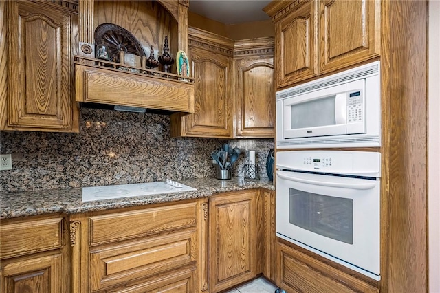 kitchen featuring white appliances, decorative backsplash, and dark stone countertops