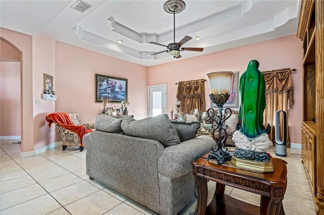 living room with light tile patterned flooring, ceiling fan, and a tray ceiling