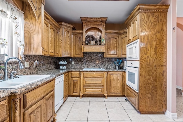 kitchen featuring tasteful backsplash, sink, dark stone countertops, light tile patterned floors, and white appliances