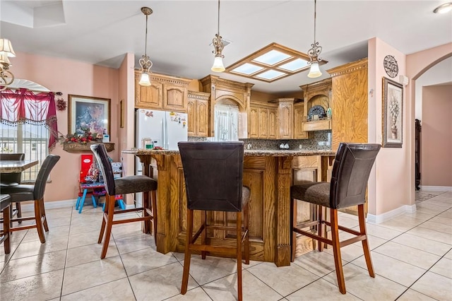 kitchen featuring pendant lighting, backsplash, white fridge with ice dispenser, light tile patterned floors, and kitchen peninsula