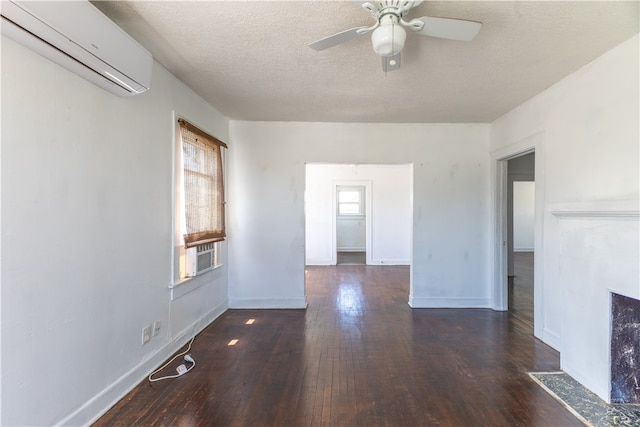 spare room featuring dark wood-type flooring, a wall unit AC, a textured ceiling, and ceiling fan