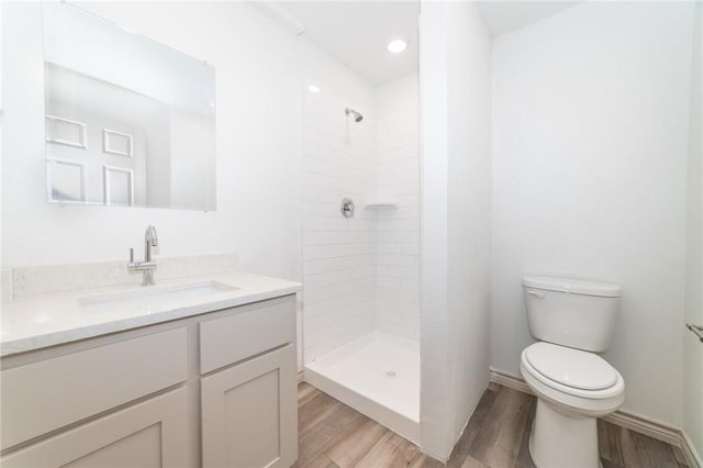 bathroom with tiled shower, wood-type flooring, toilet, and vanity