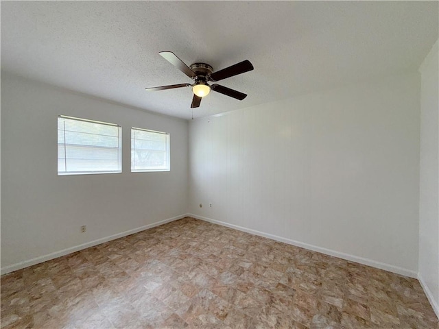 empty room with a textured ceiling, a ceiling fan, and baseboards