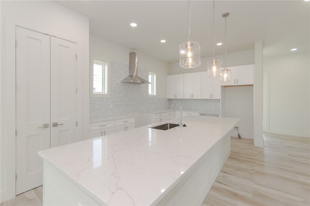 kitchen featuring wall chimney exhaust hood, sink, a kitchen island with sink, and decorative light fixtures