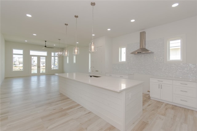 kitchen with light hardwood / wood-style flooring, a wealth of natural light, wall chimney exhaust hood, and a spacious island