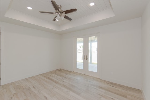 empty room featuring french doors, ceiling fan, a raised ceiling, and light wood-type flooring