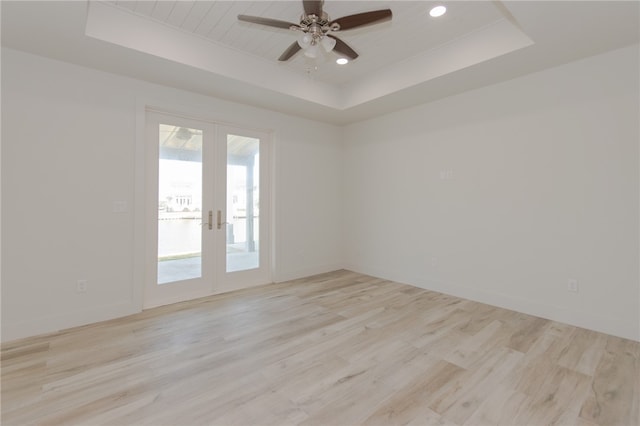 empty room featuring ceiling fan, a tray ceiling, french doors, and light hardwood / wood-style floors