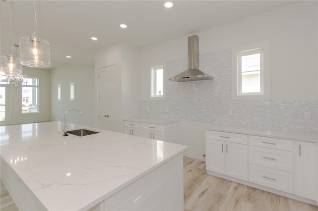 kitchen featuring sink, decorative light fixtures, wall chimney exhaust hood, and a center island with sink