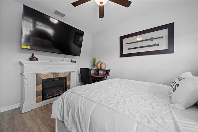 bedroom featuring light wood-type flooring, a fireplace, and ceiling fan