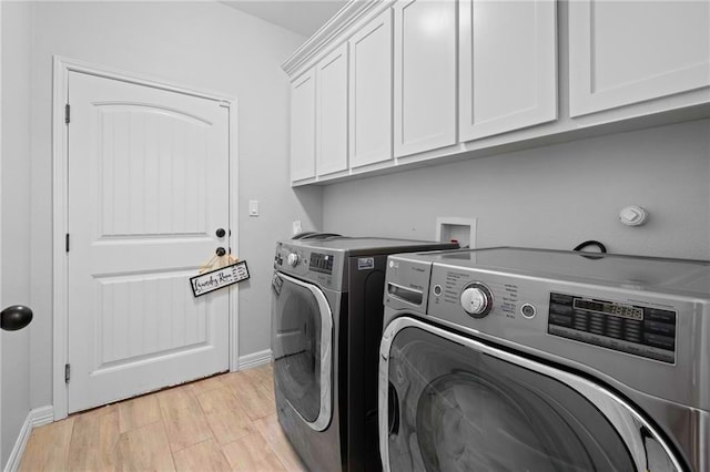 clothes washing area with washing machine and dryer, cabinets, and light hardwood / wood-style flooring