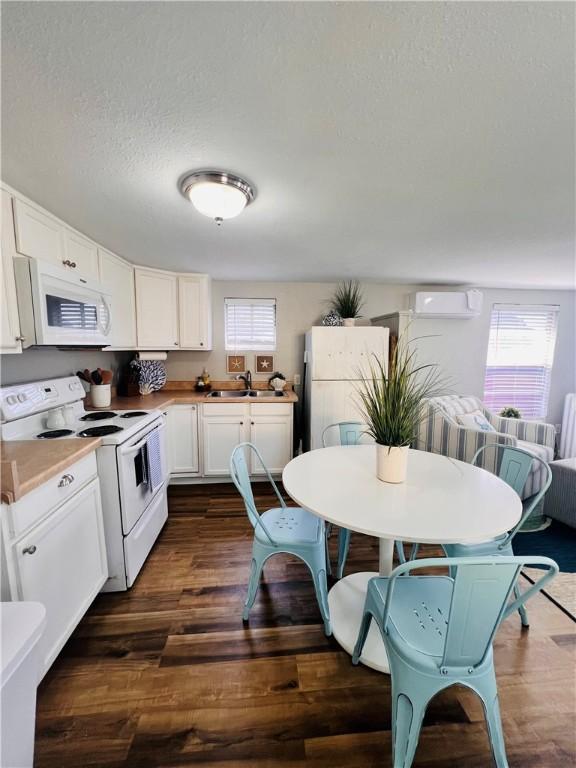 402 E Nopal St, Rockport, TX 78382 - kitchen with a wall unit AC, white appliances, dark wood-style floors, and white cabinetry