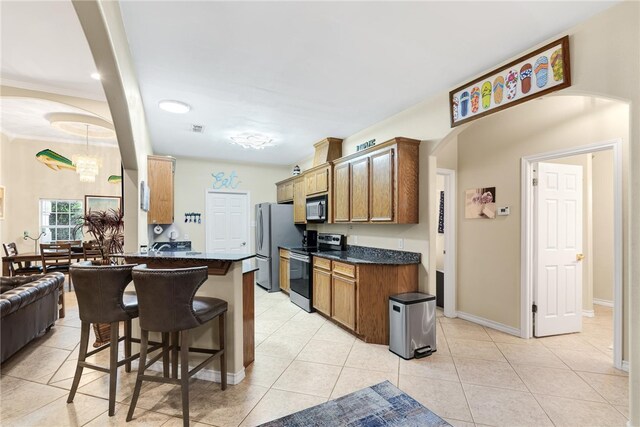 kitchen with stainless steel appliances, kitchen peninsula, a kitchen breakfast bar, light tile patterned floors, and a chandelier