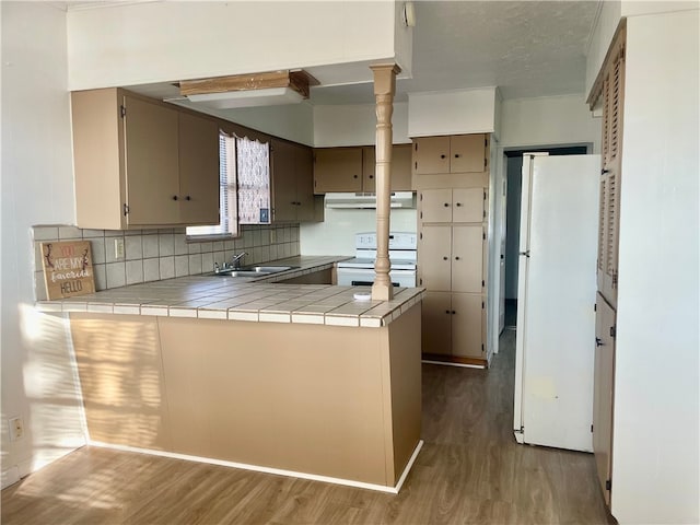 kitchen with kitchen peninsula, white appliances, hardwood / wood-style flooring, tile counters, and range hood