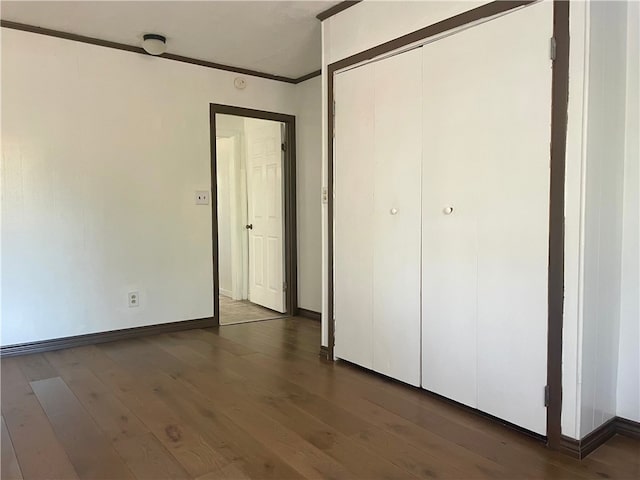 unfurnished bedroom with crown molding, dark wood-type flooring, and a closet