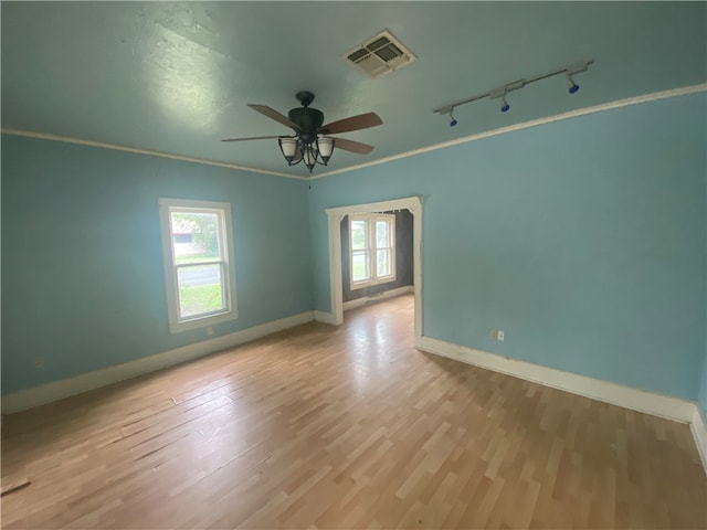 empty room featuring ceiling fan, a healthy amount of sunlight, light wood-type flooring, and crown molding